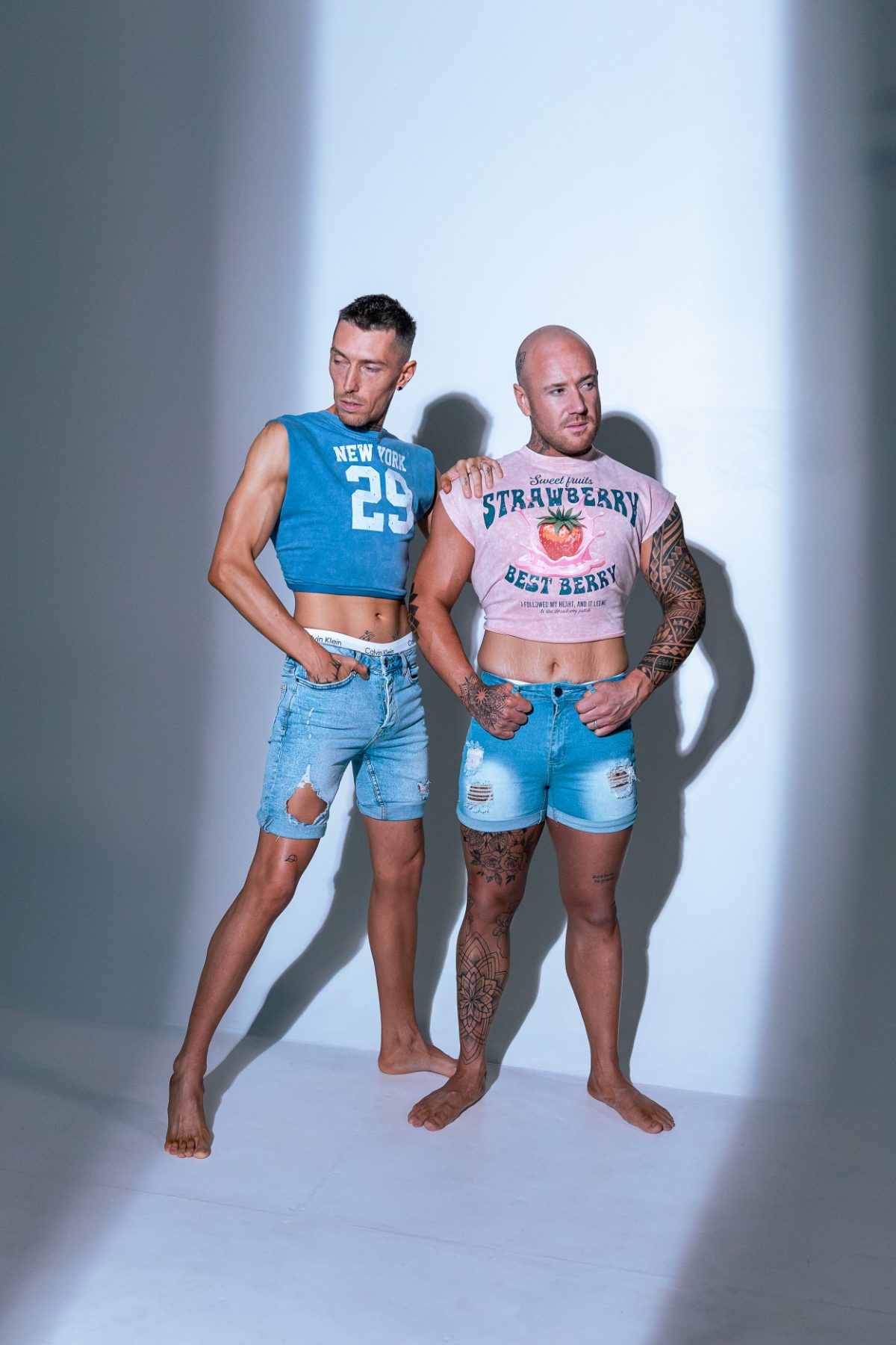 Two Elevate clients posing together in the studio in denim shorts and crop tops, lit by a single spotlight