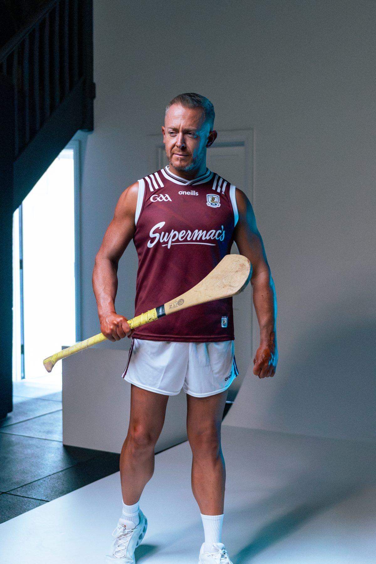 A client photographed fully clothed in a Galway GAA jersey and shorts, holding a hurley on the studio set